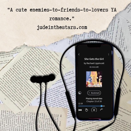 On a backdrop of book pages, an iPhone with the cover of She Gets the Girl by Rachael Lippincott & Alyson Derrick, narrated by Natalie Naudus & Valentina Ortiz. At the top of the image, a strip of torn paper with a quote: "A cute enemies-to-friends-to-lovers YA romance." and a URL: judeinthestars.com.