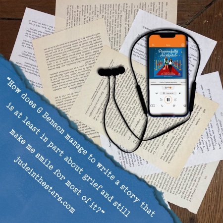On a backdrop of book pages, an iPhone with the cover of Purposefully Accidental by G Benson, narrated by Quinn Riley. In the bottom left corner of the image, a strip of torn paper with a quote: "How does G Benson manage to write a story that is at least in part about grief and still make me smile for most of it?" and a URL: judeinthestars.com.